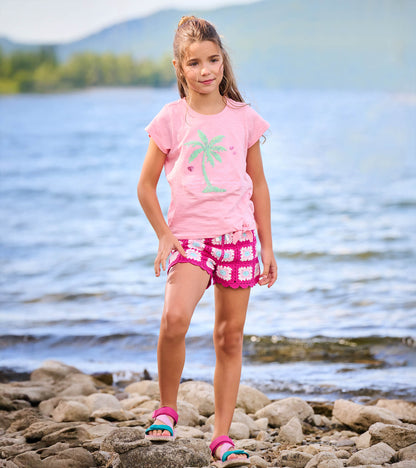 Girl wearing a pink short sleeve tie-front T-shirt with palm tree graphic by the water