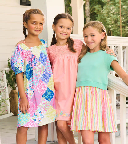 Girls wearing colorful summer dresses, including a patchwork print dress, a pink dress, and a mint top with striped skirt