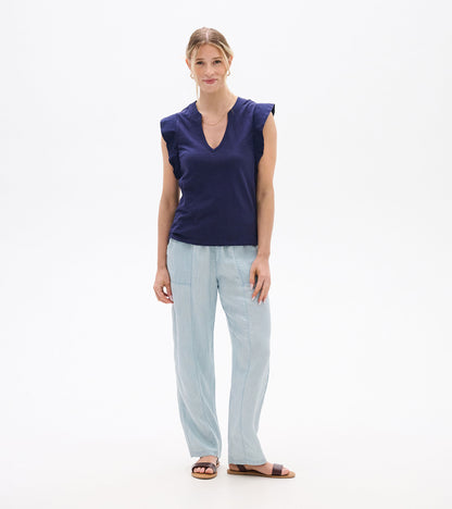 Woman wearing a navy sleeveless V-neck tank top with ruffled shoulders and light blue pants, front view