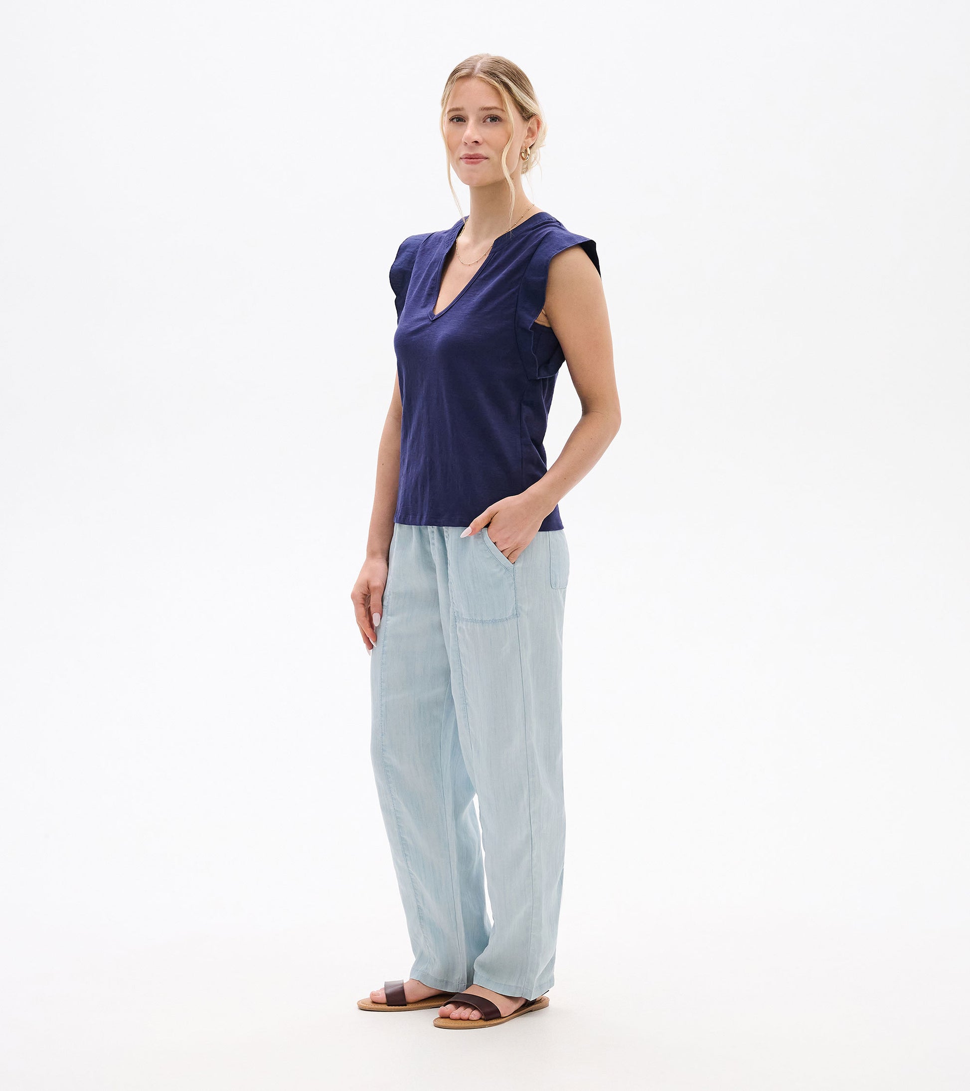 Woman wearing a navy sleeveless V-neck tank top with ruffled shoulders and light blue pants, front view