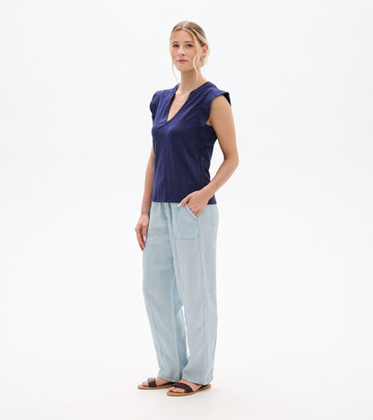 Woman wearing a navy sleeveless V-neck tank top with ruffled shoulders and light blue pants, front view