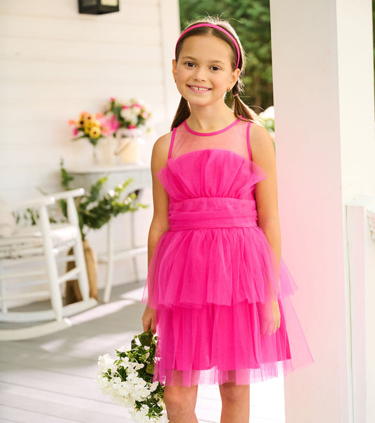 Girl wearing a fuchsia sleeveless tulle party dress with sheer neckline, ruched waist, and tiered skirt