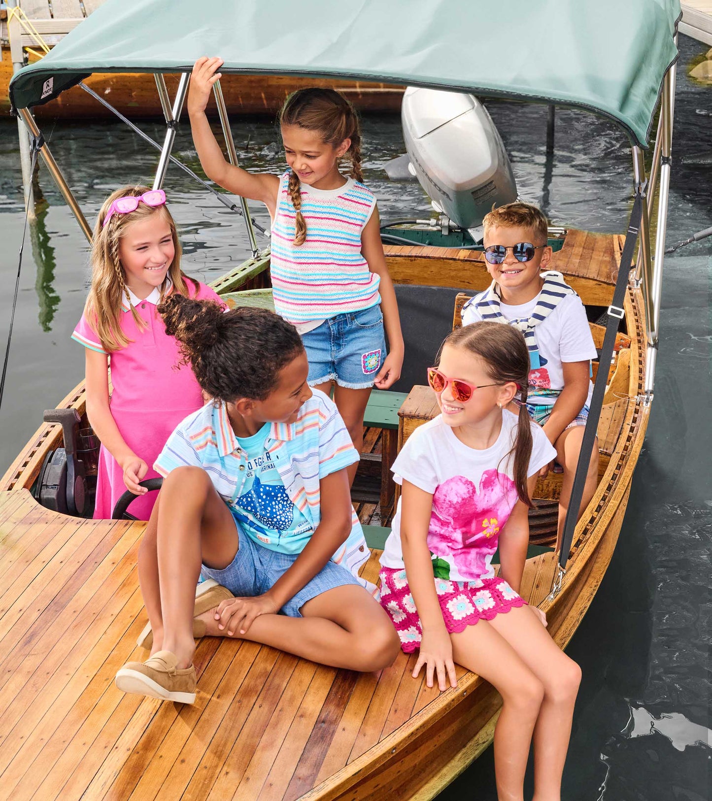 Girls wearing colorful summer tops and shorts sitting on a wooden boat under a canopy