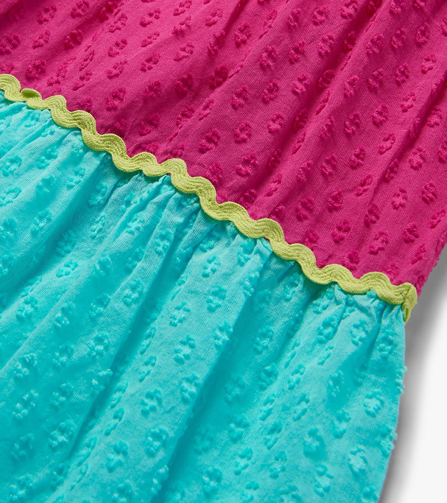 Close-up of a pink and turquoise textured color block dress with lime green scalloped trim.