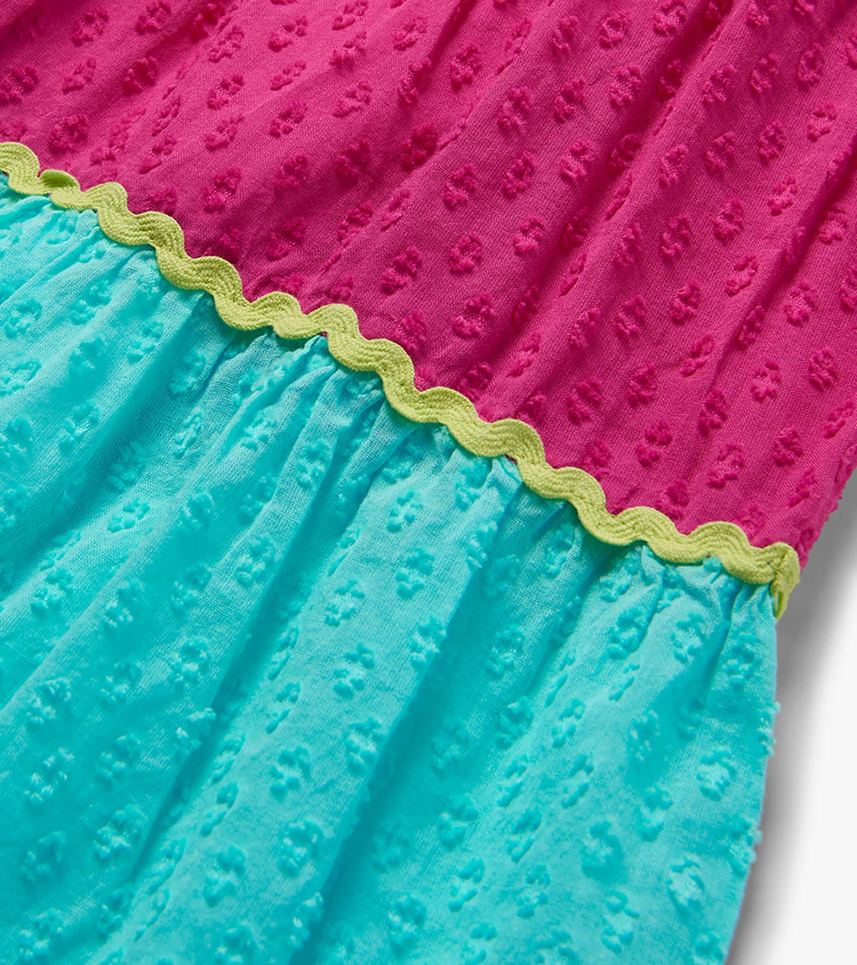Close-up of a pink and turquoise textured color block dress with lime green scalloped trim.