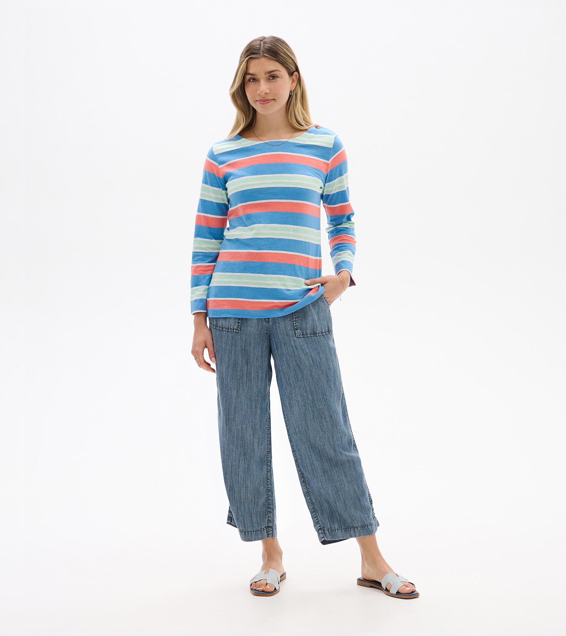 Woman wearing a long-sleeve blue, coral, and mint striped Breton top with a scoop neck, front view