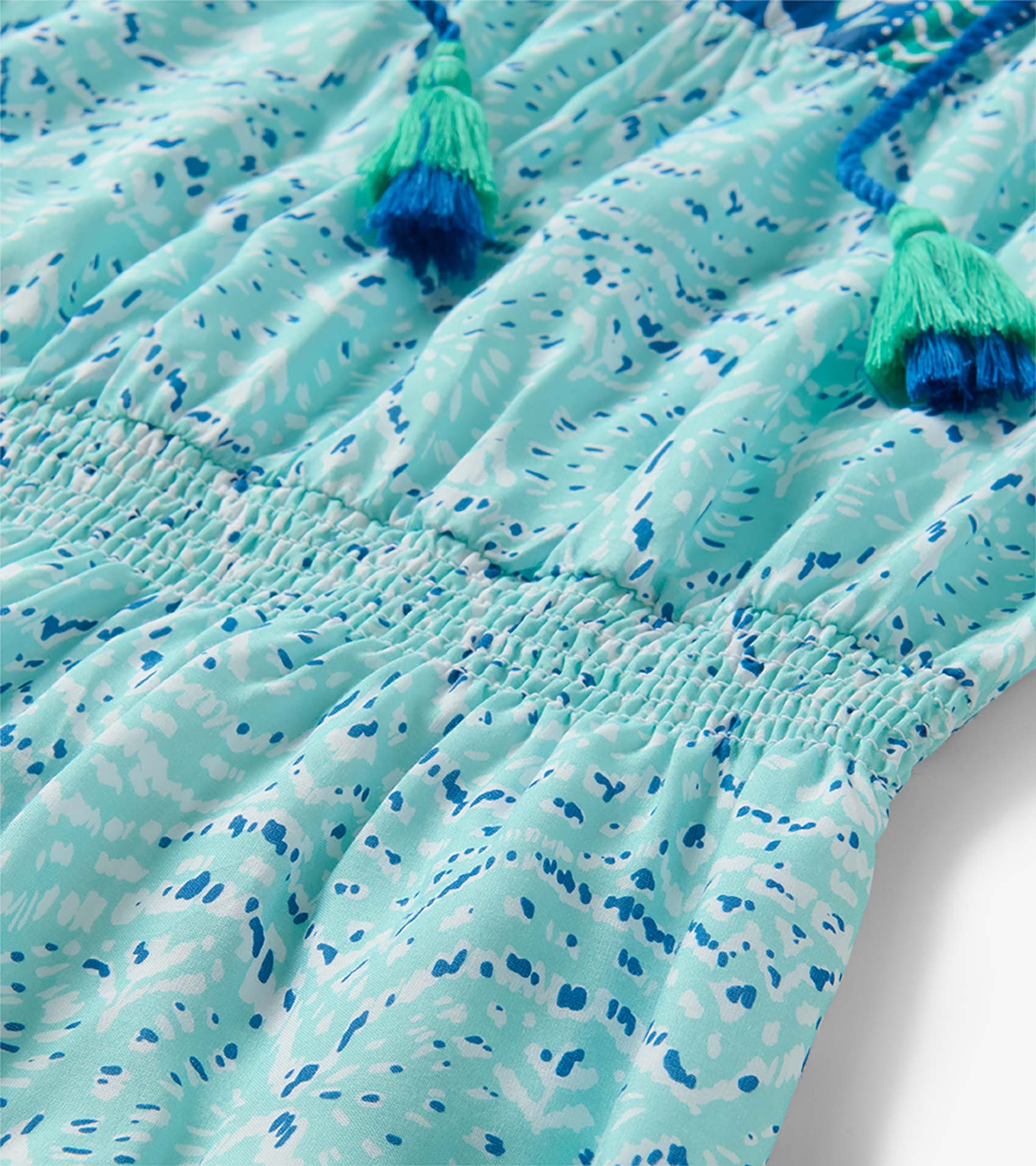 Close-up of a mint and blue ikat-print dress with smocked waist and tassel ties
