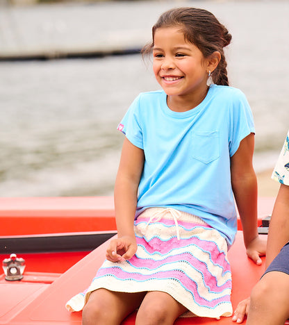 Girl wearing a pastel striped crochet skirt with wavy scalloped hem and drawstring waist, seated outdoors