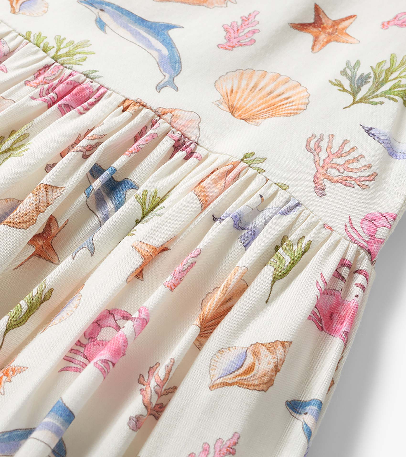 Cream girls dress with colorful seashell, coral, and dolphin print and gathered smocked waist detail