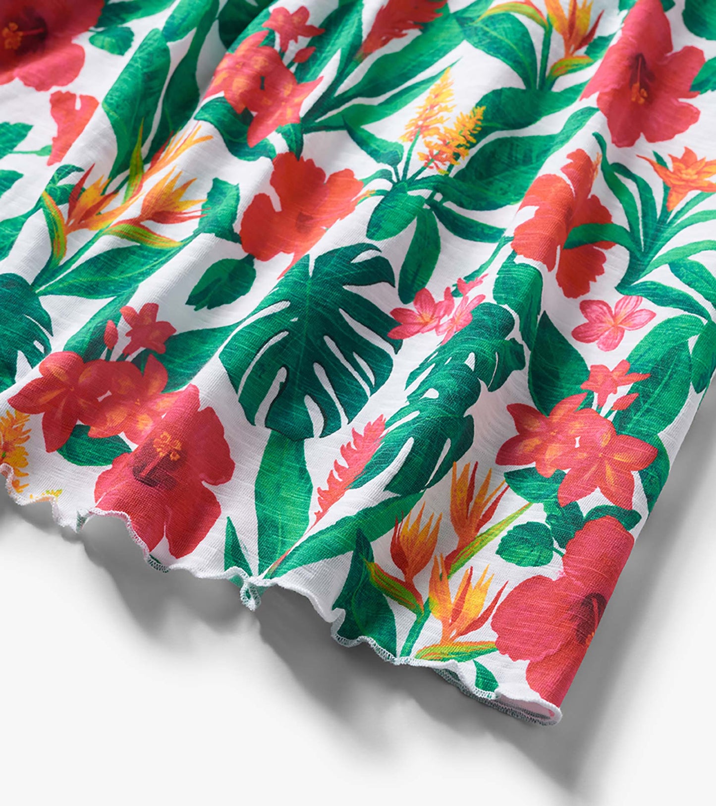 White girls' trapeze dress with tropical floral and green leaf print, shown in close-up fabric detail