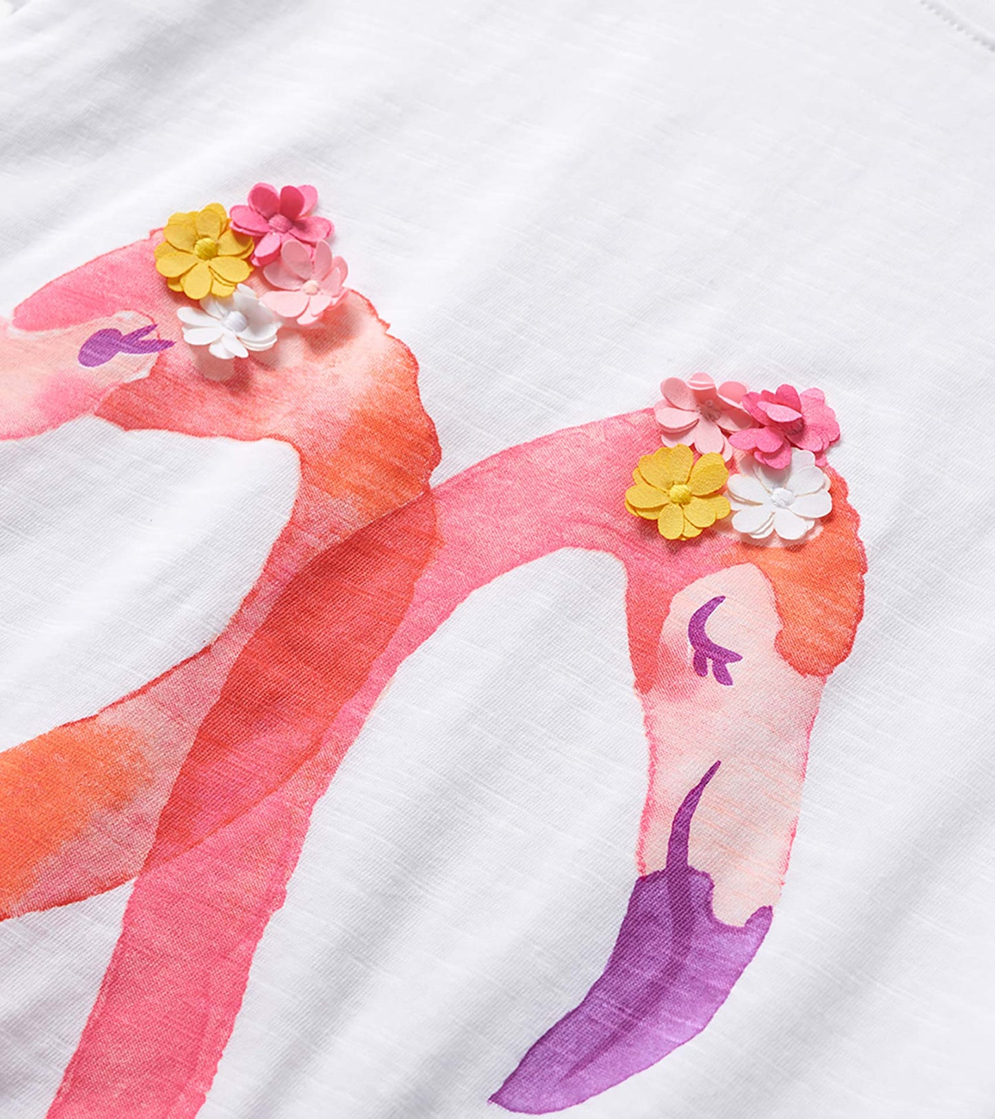 White girls graphic tee with pink flamingos and colorful flower appliqués on the print, close-up view