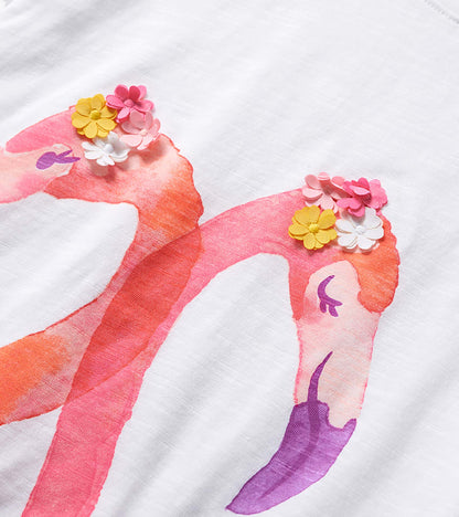 White girls graphic tee with pink flamingos and colorful flower appliqués on the print, close-up view
