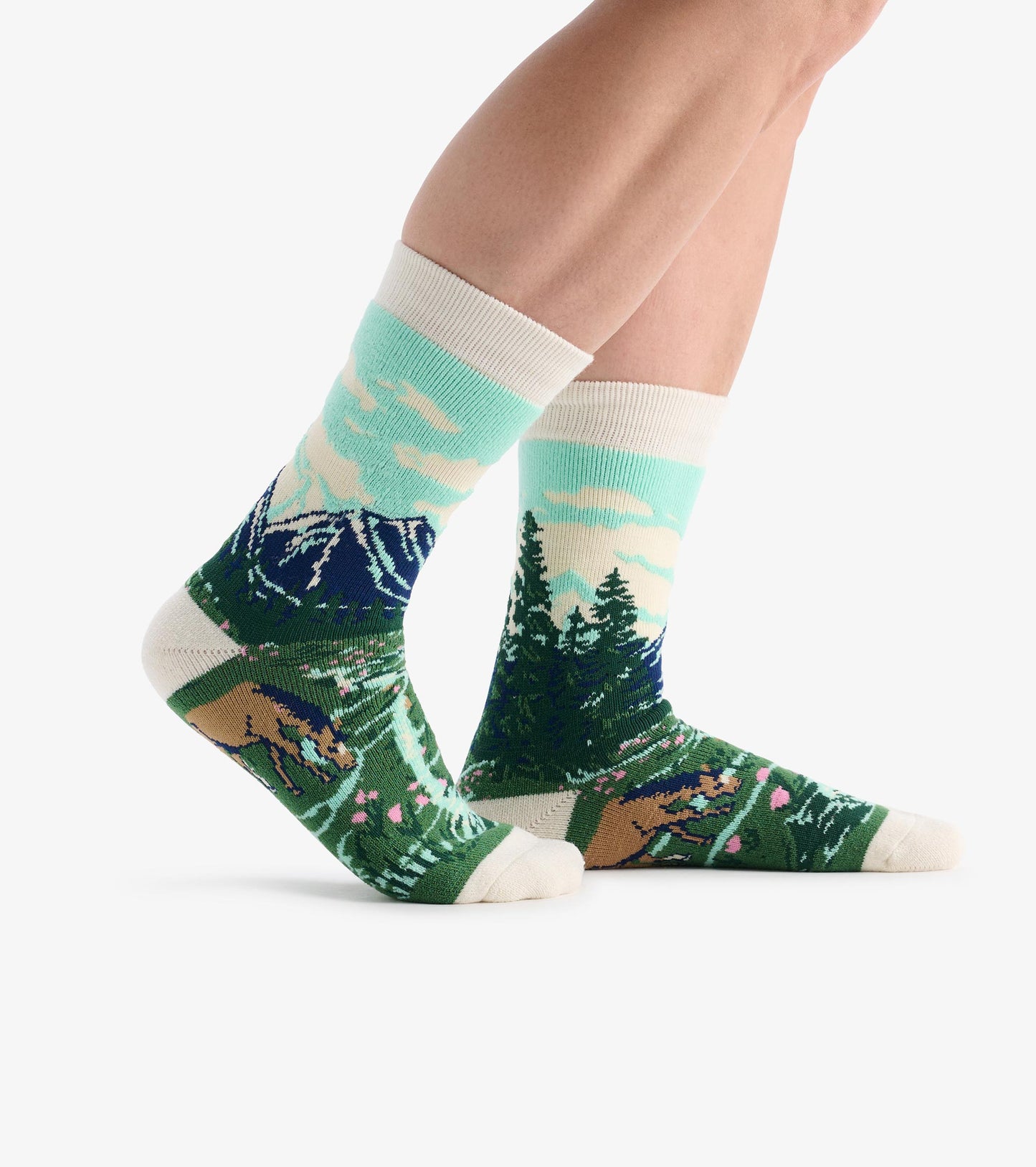 Crew socks with mountain, forest and bear pattern in green, blue and cream, shown on legs in side view.