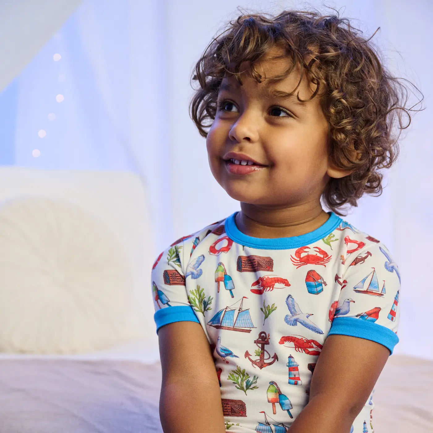 Promotes kids sleepwear. Showing smiling child sitting on a bed wearing nautical print pajamas.