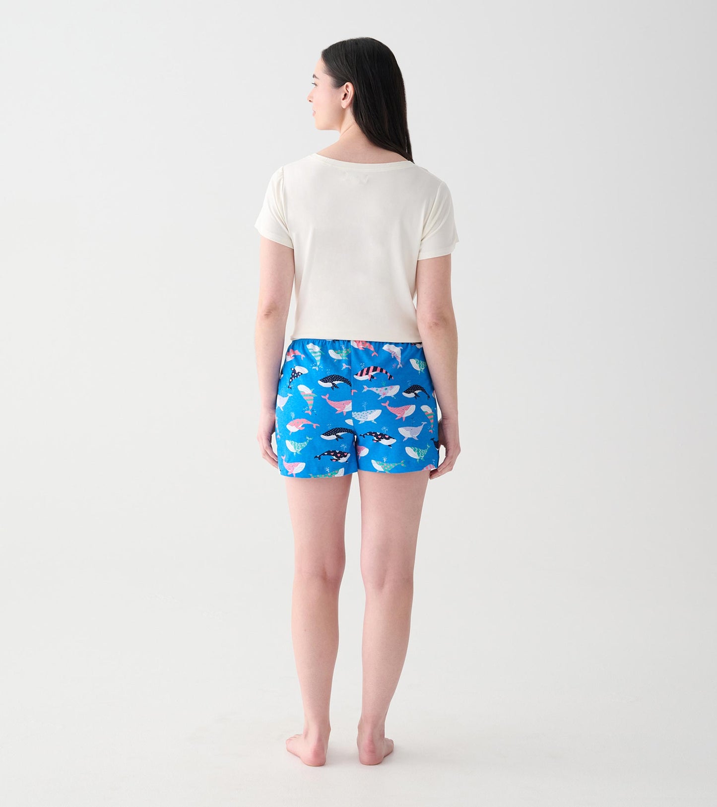 Women's cream V-neck T-shirt back view on a model, paired with blue whale-print shorts