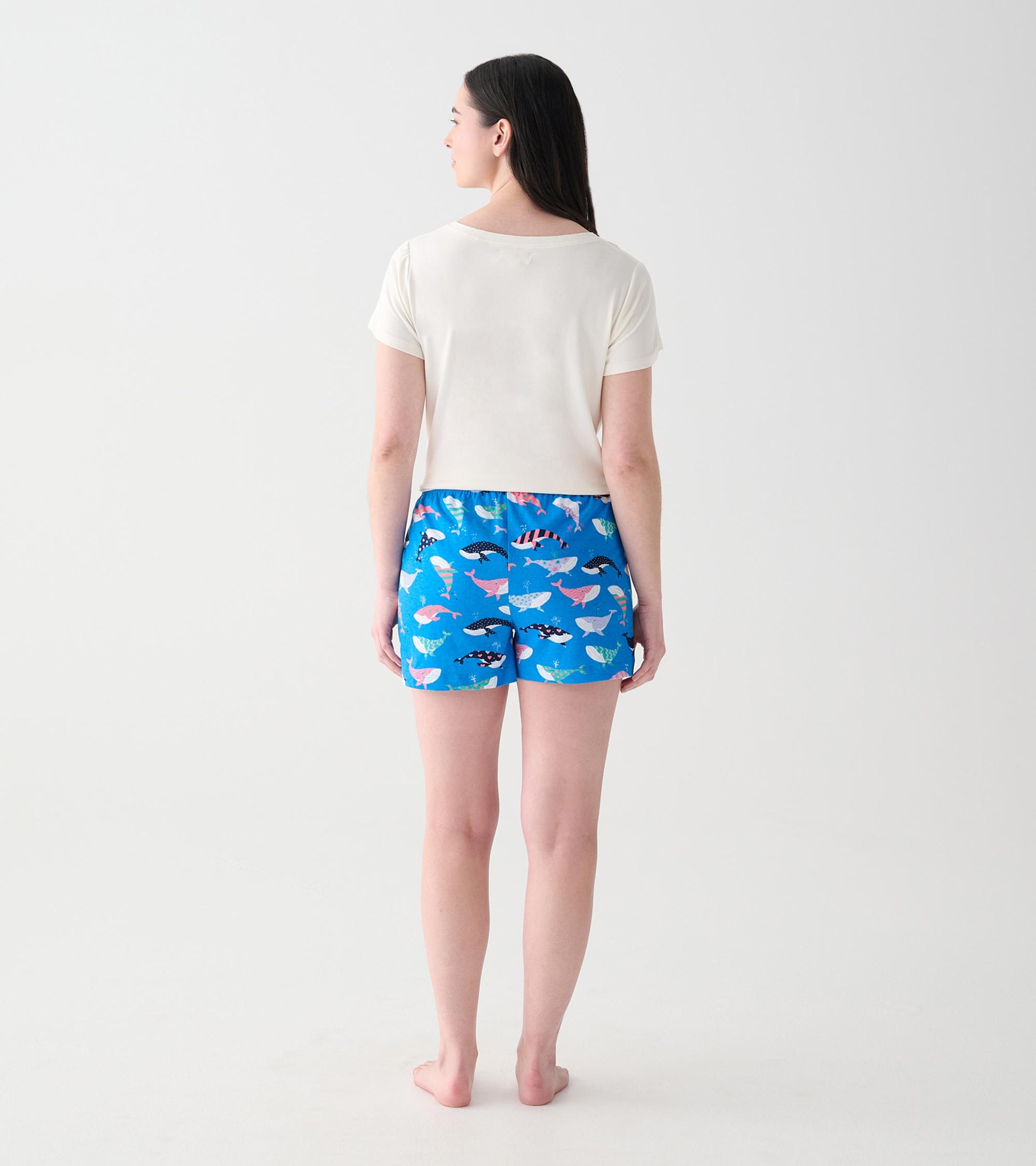 Women's cream V-neck T-shirt back view on a model, paired with blue whale-print shorts