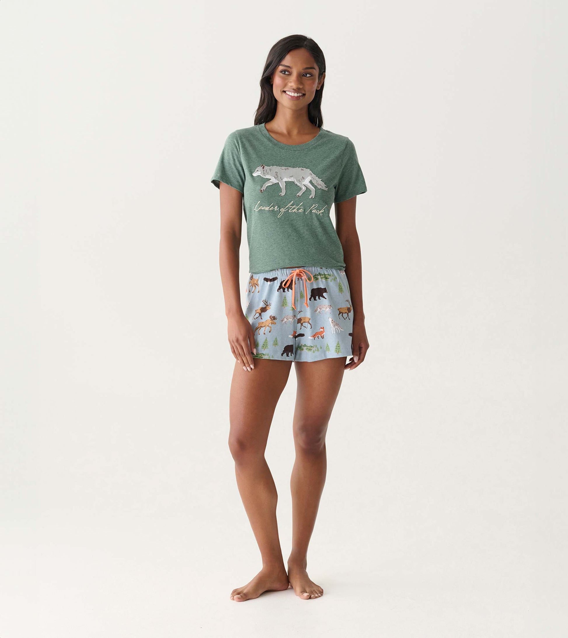 Green short-sleeve pajama T-shirt with wolf graphic and text, paired with light blue animal-print shorts on model