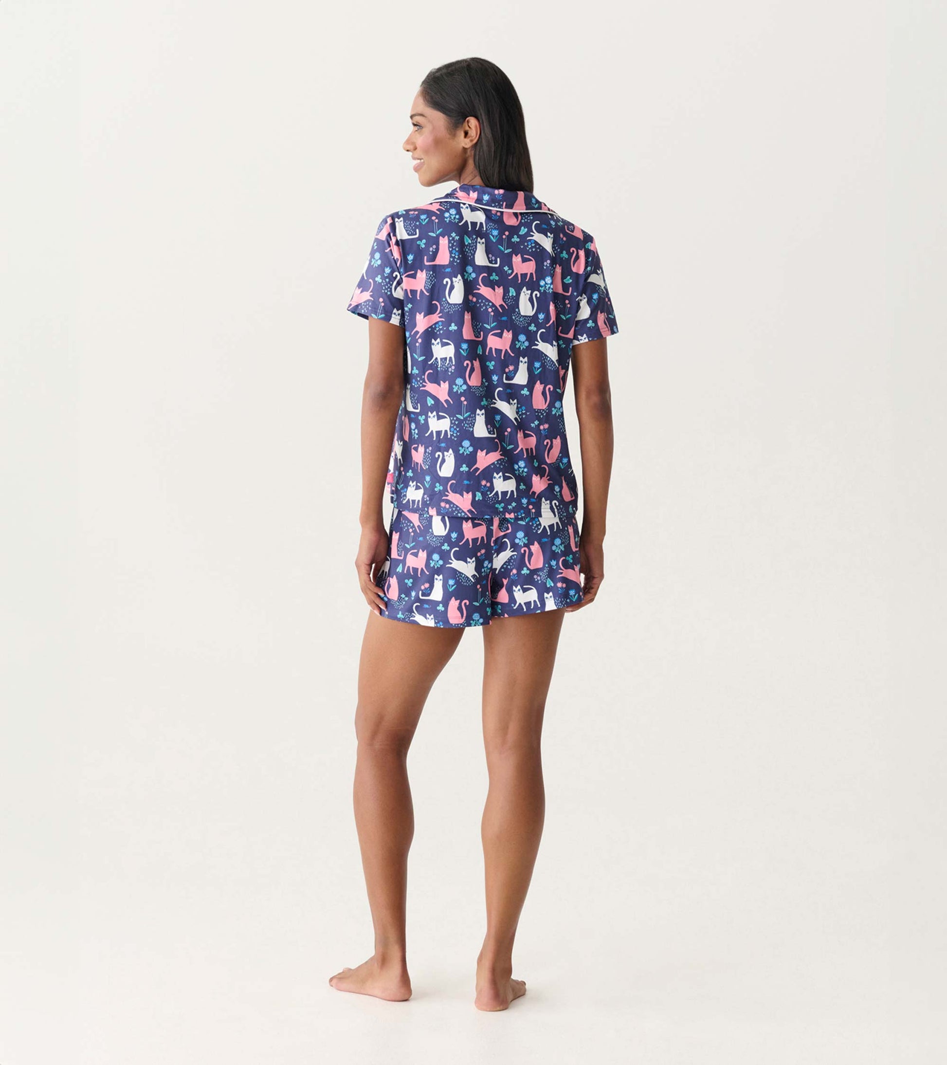 Back view of a navy short-sleeve pajama set with pink and white cat print, matching shorts, and button-down top.