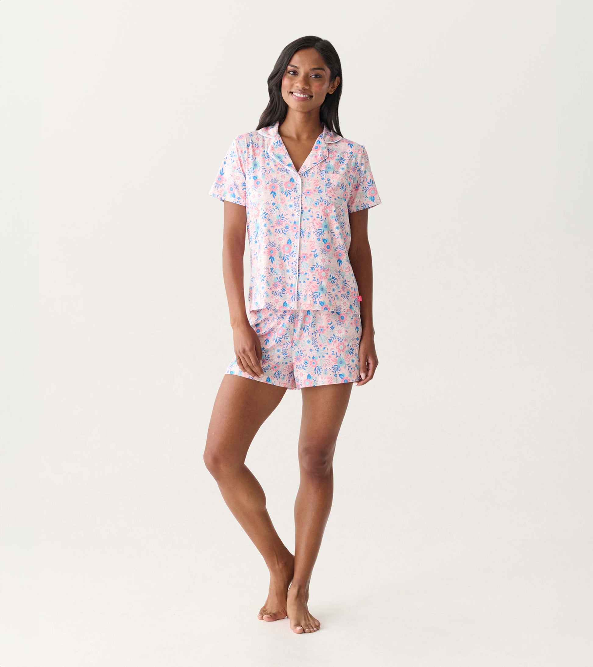 Woman wearing a pink and blue floral short-sleeve button-down pajama set with shorts, front view.