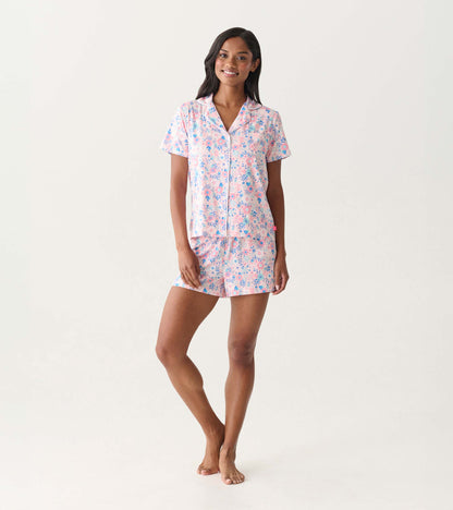 Woman wearing a pink and blue floral short-sleeve button-down pajama set with shorts, front view.