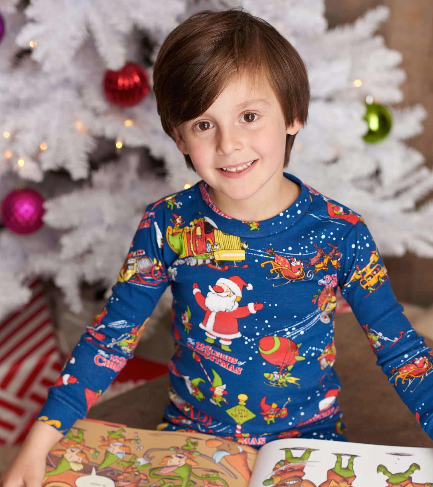 Blue long-sleeve pajama set featuring colorful Christmas-themed graphics, worn by a child sitting with a book.