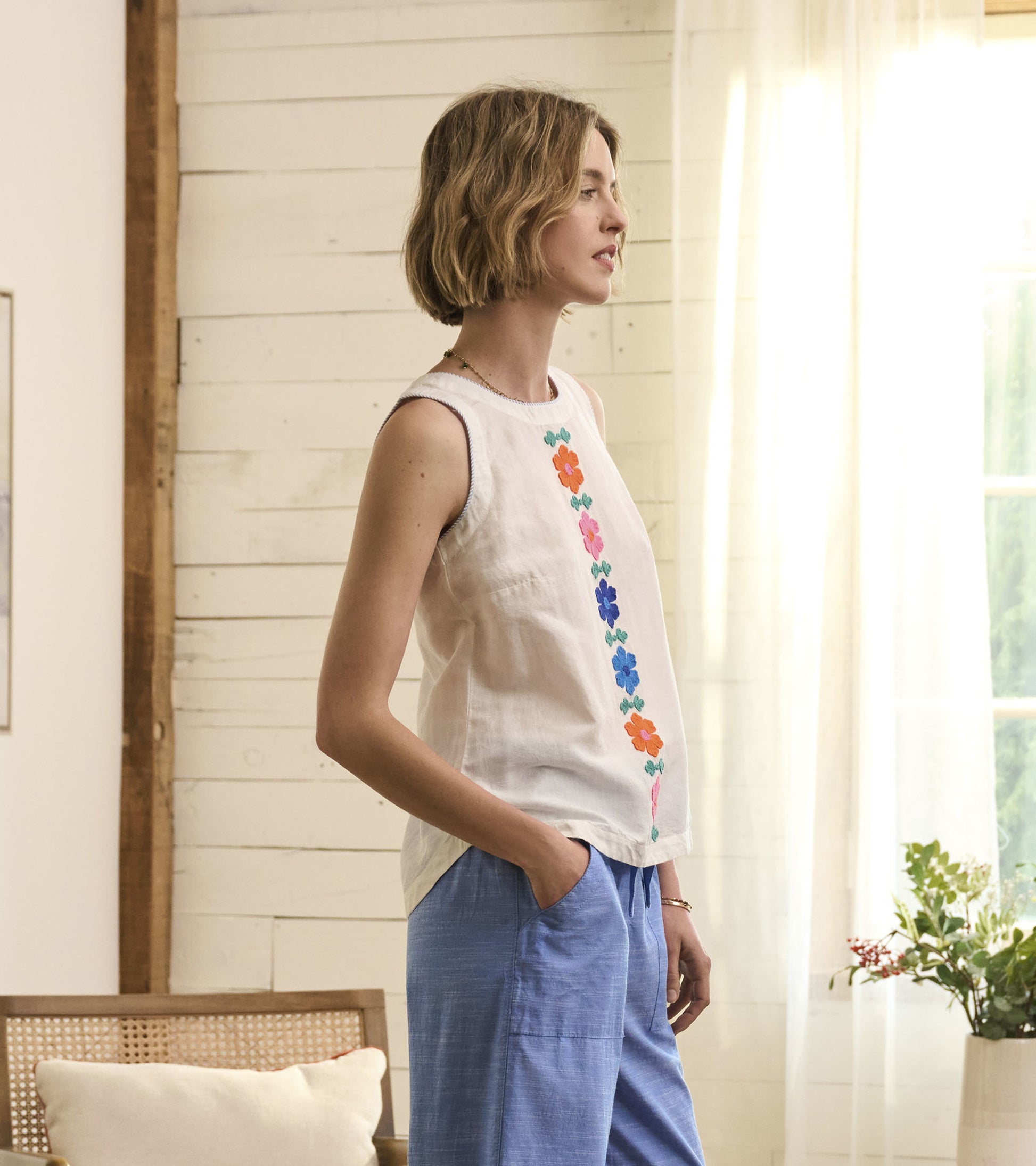 White sleeveless tank top featuring colorful embroidered flowers, styled with light blue pants.
