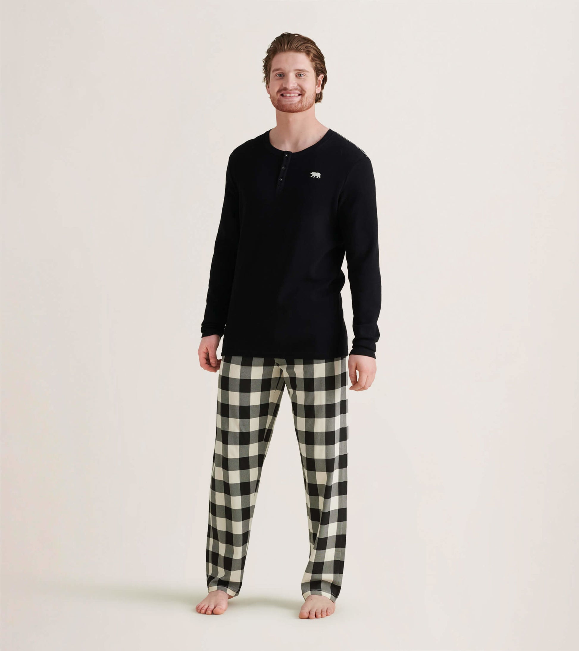 Men's black waffle henley shirt paired with black and white checkered pajama pants, standing barefoot.