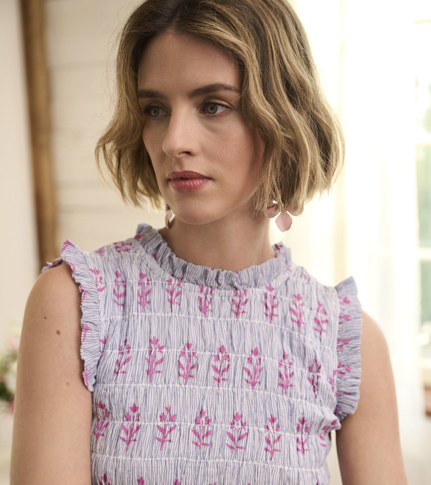 Smocked maxi dress in blue and white seersucker with pink floral pattern and ruffled sleeves.