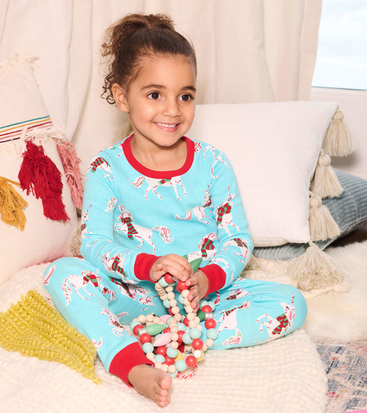 Light blue organic cotton pajama set featuring festive unicorns, red trim, and a relaxed fit, worn by a smiling child.