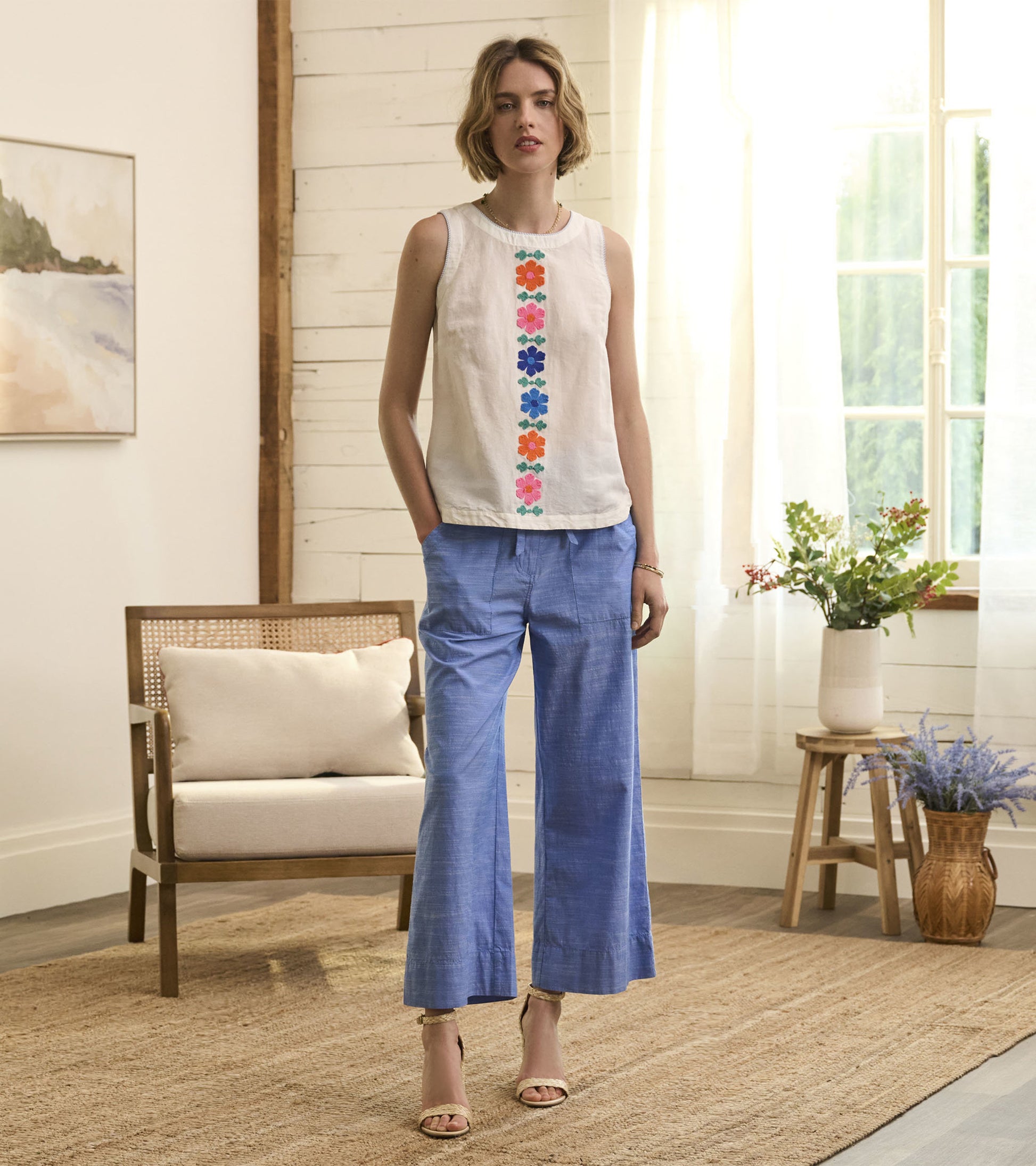 White sleeveless tank top featuring colorful embroidered flowers down the center, paired with light blue wide-leg pants.