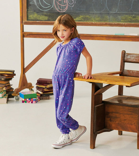 Purple jumpsuit with colorful heart pattern, short puff sleeves, and elastic waist, styled with white sneakers.