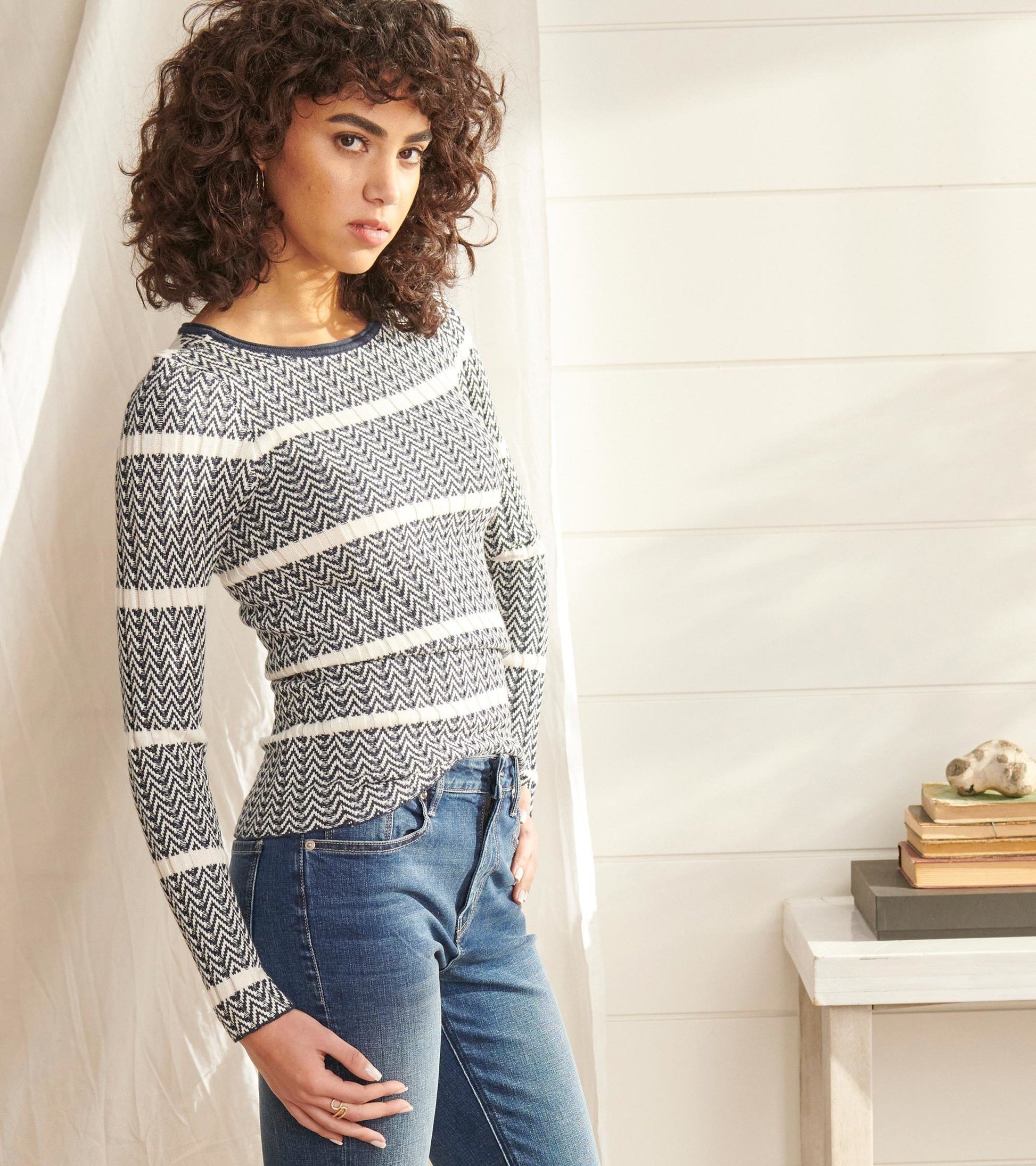 Zigzag patterned sweater in navy and white, featuring long sleeves and a fitted silhouette, paired with blue jeans.