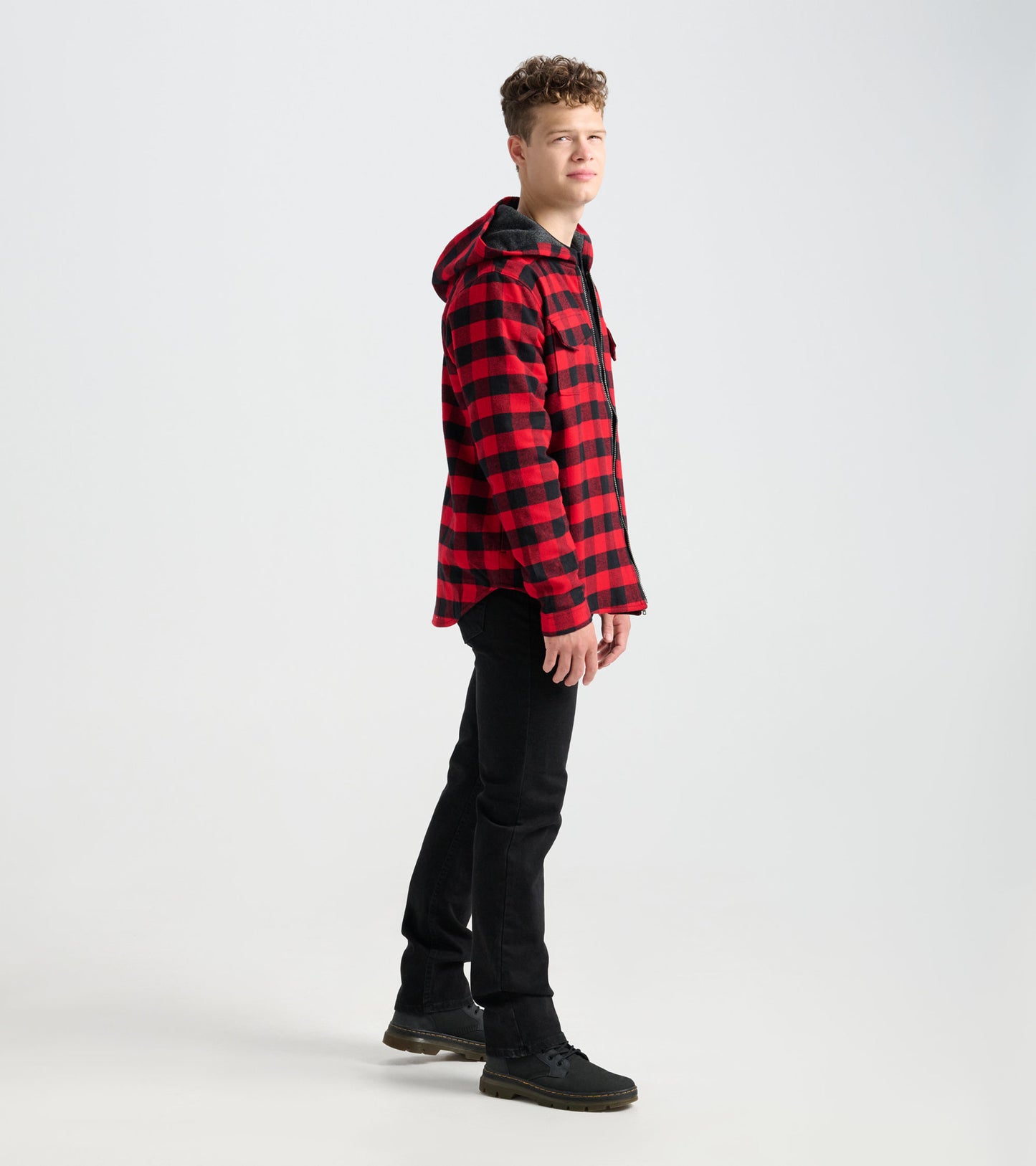 Red and black plaid flannel jacket with a hood, worn by a model standing sideways, paired with black jeans.