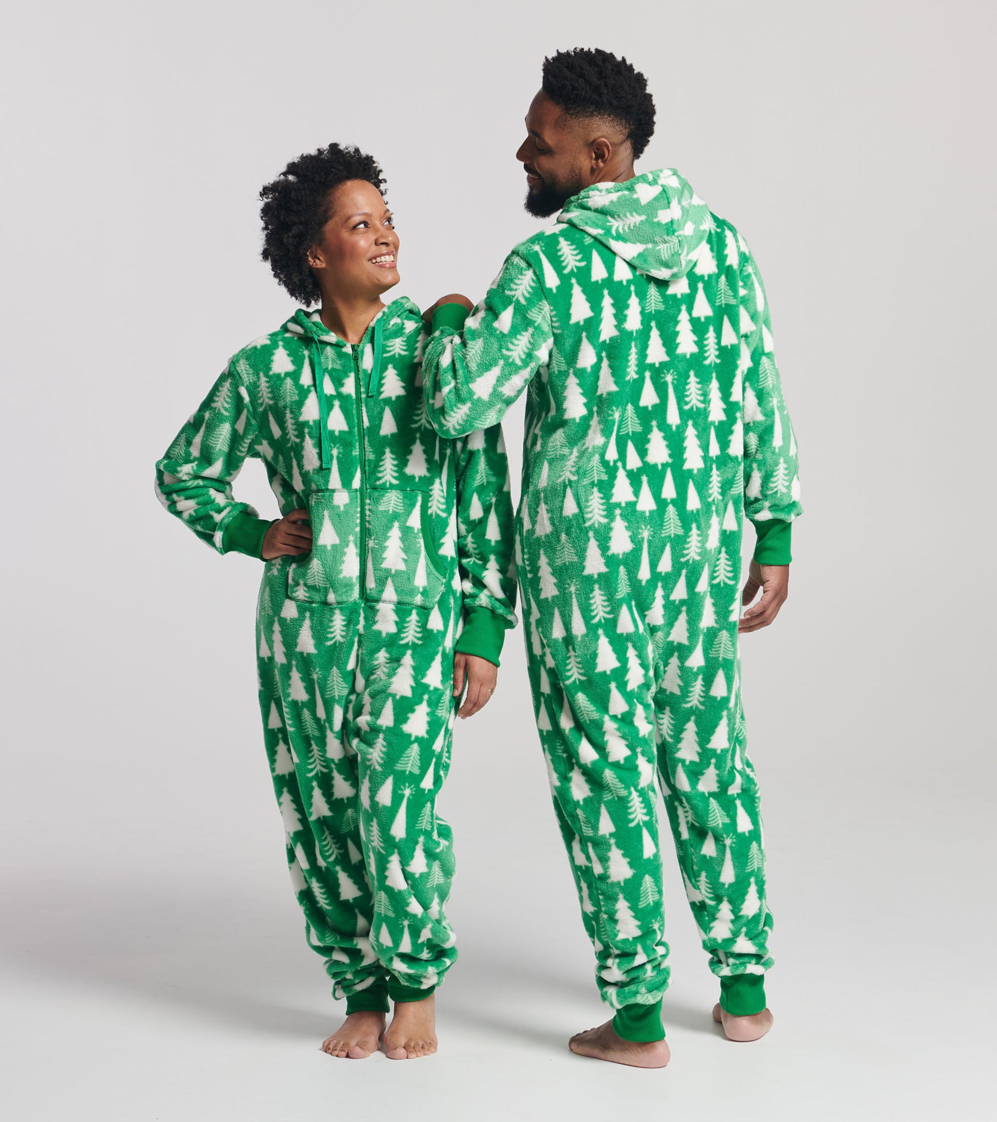 Green hooded fleece jumpsuit featuring a white tree pattern, worn by two people standing side by side.