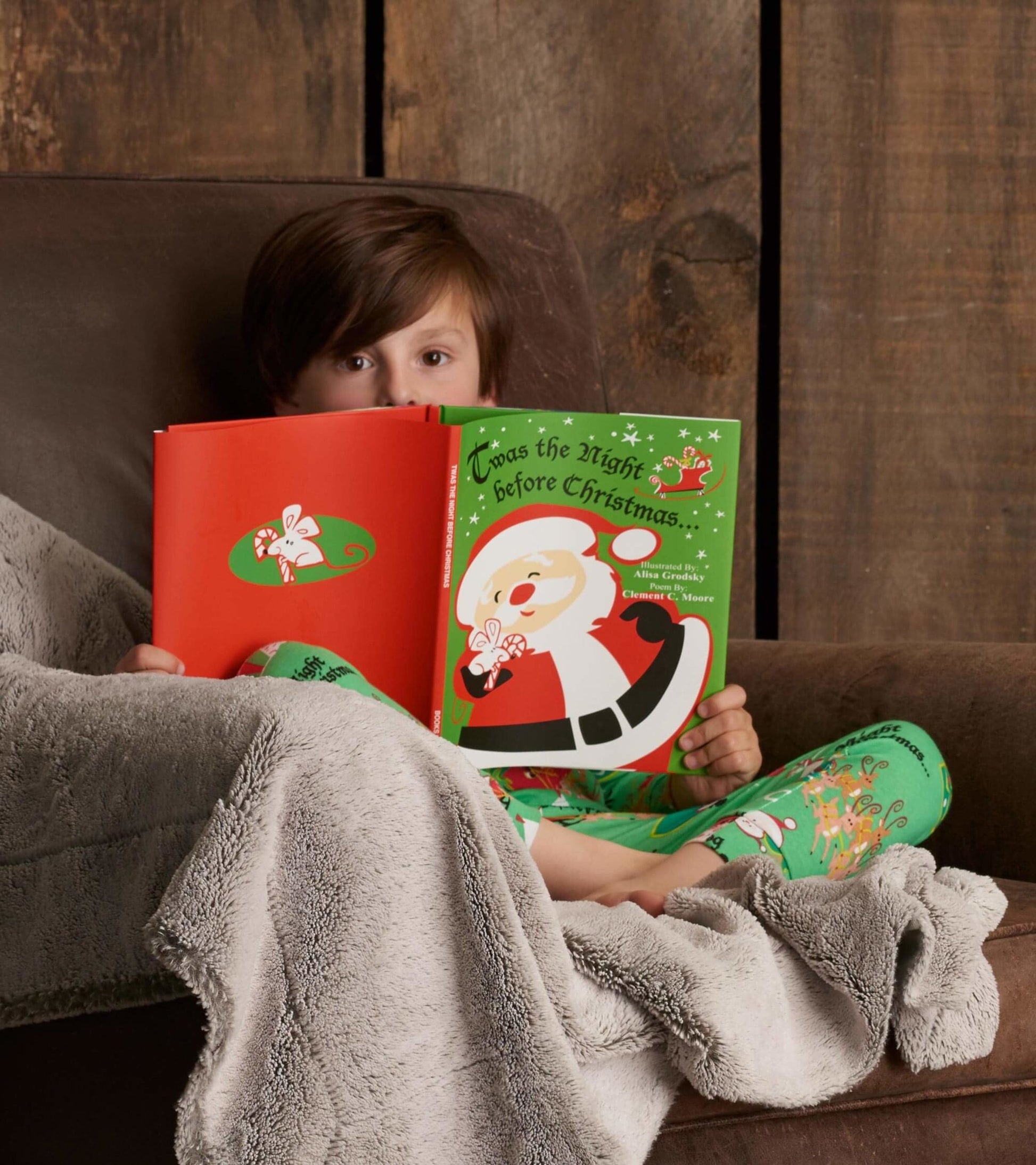 Green pajama set with festive Christmas patterns, worn by a child reading a holiday book while cozy on a couch.