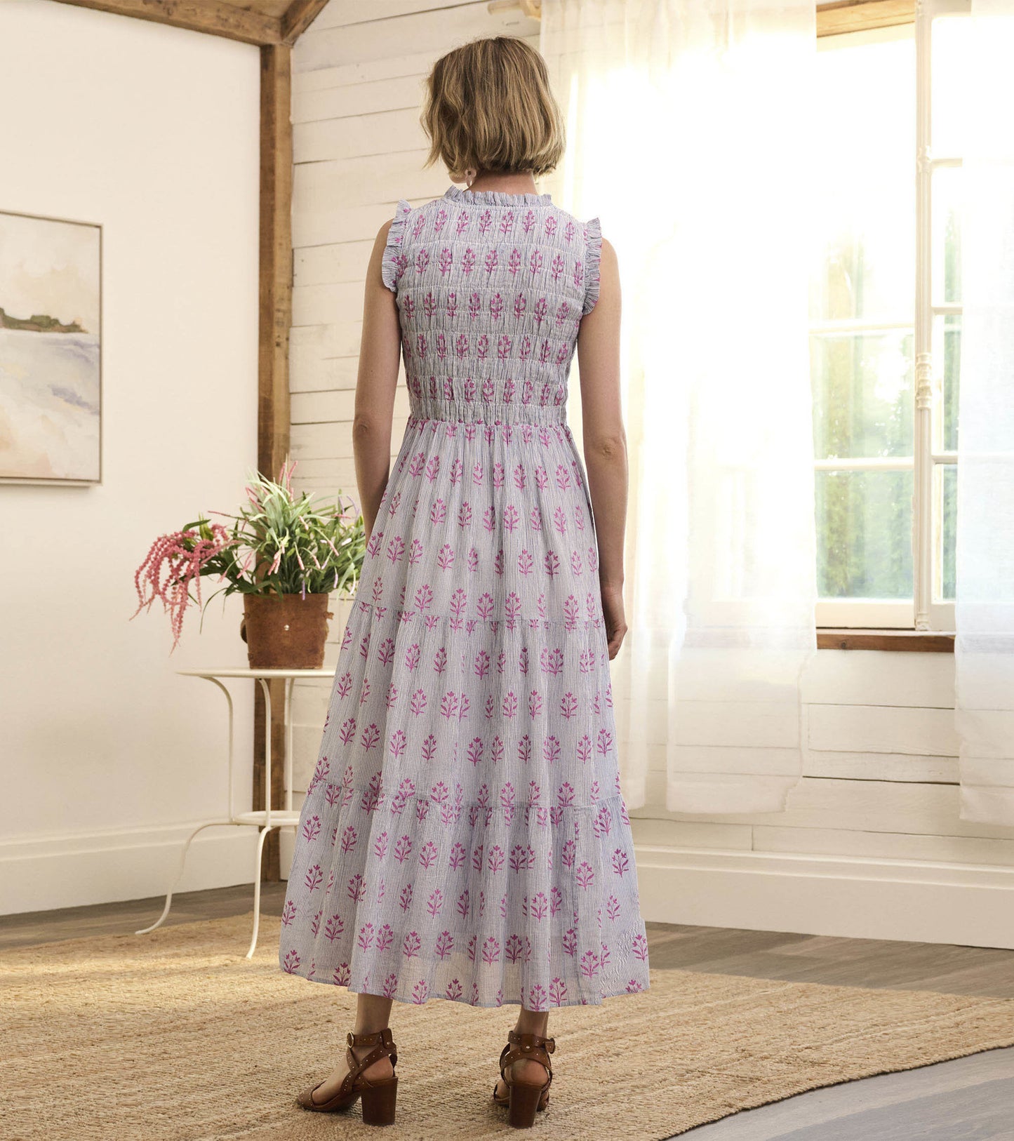 Back view of a smocked maxi dress in light blue with pink floral patterns, featuring ruffled sleeves and a tiered skirt.