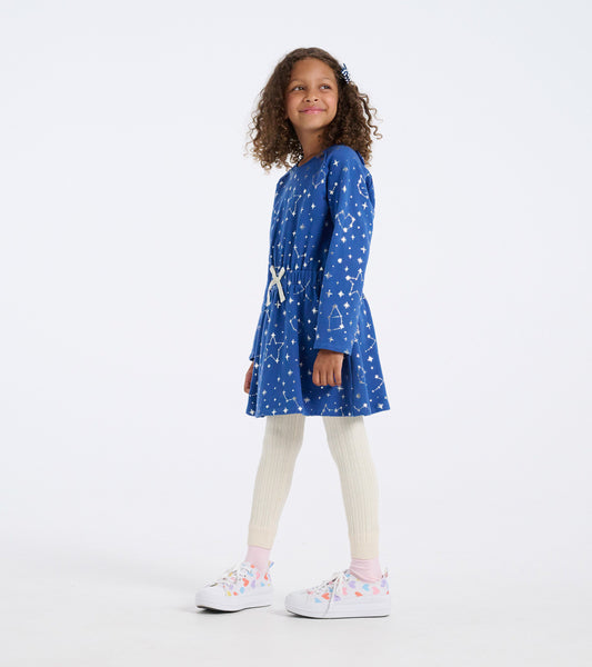 Blue terry dress with white constellation pattern, cinched waist, long sleeves, paired with cream leggings and colorful snea…