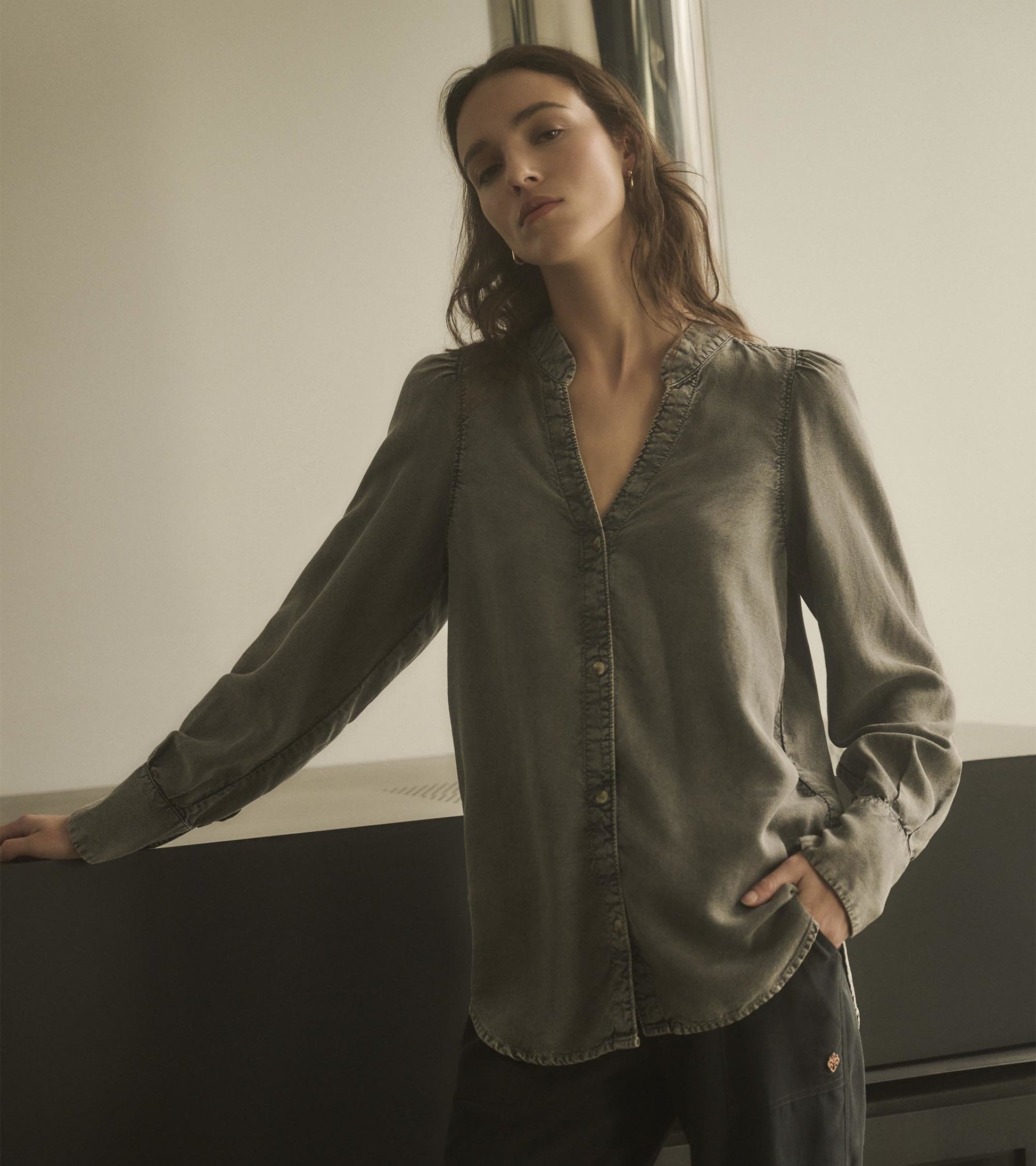 Black acid wash blouse with a V-neck, button front, and long sleeves, styled casually against a minimalist background.