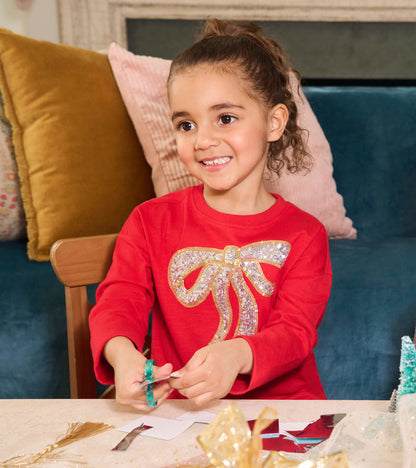Red long-sleeve dress featuring a sparkling bow design, perfect for holiday parties, worn by a girl while crafting.