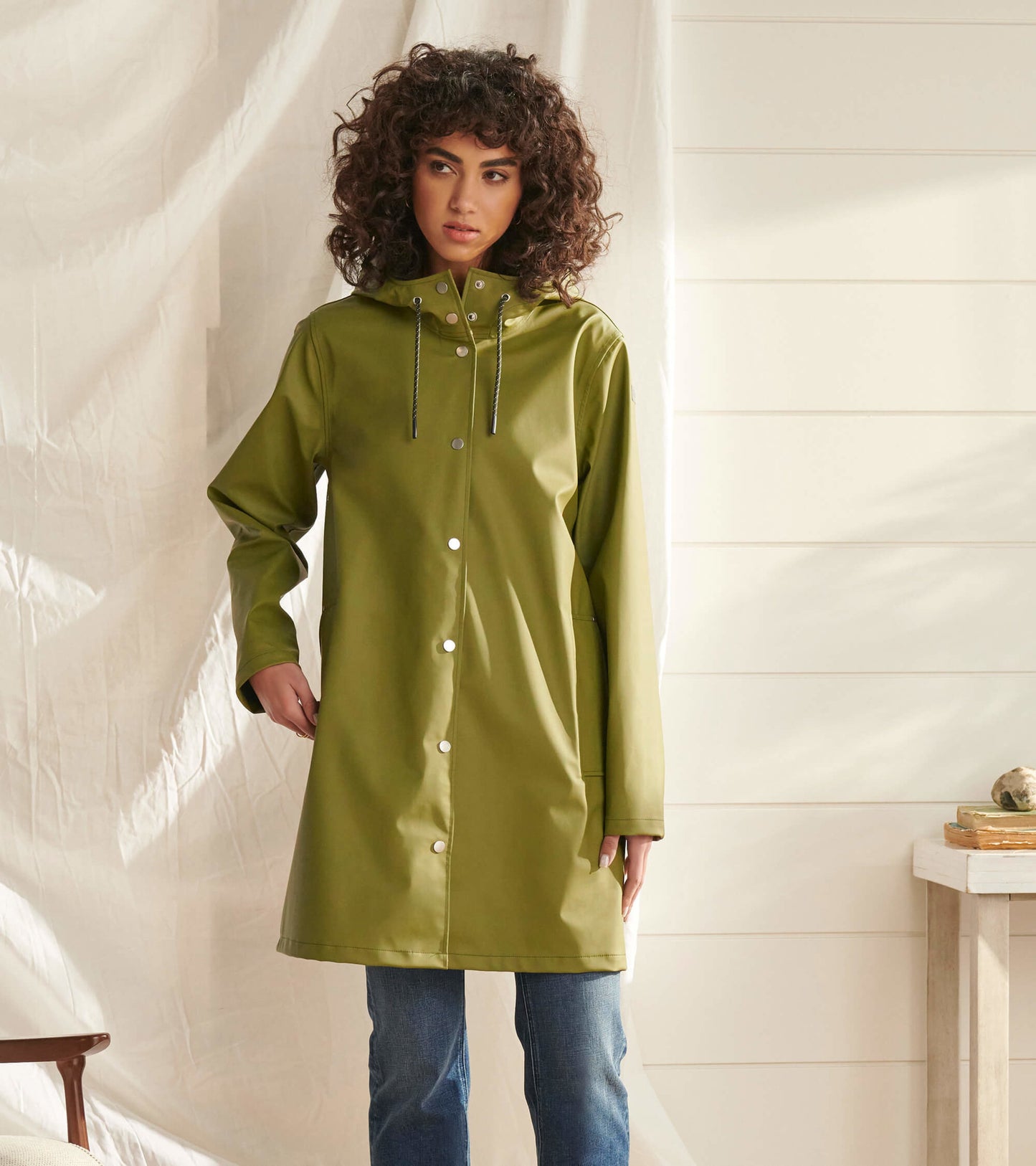 Loden green rain jacket with a hood, snap buttons, and a relaxed fit, worn over jeans.