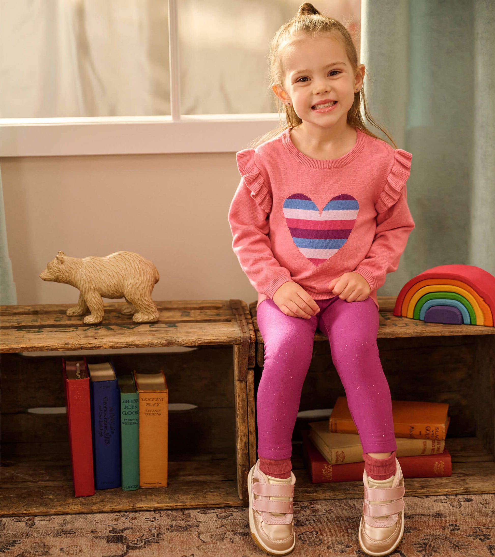 Pink sweater with ruffle sleeves and striped heart design, paired with purple leggings and gold shoes.