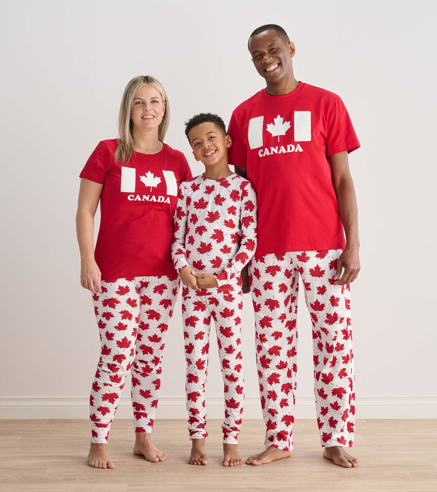 Red pajama set featuring white maple leaf patterns, suitable for kids and adults, worn by a family of three.