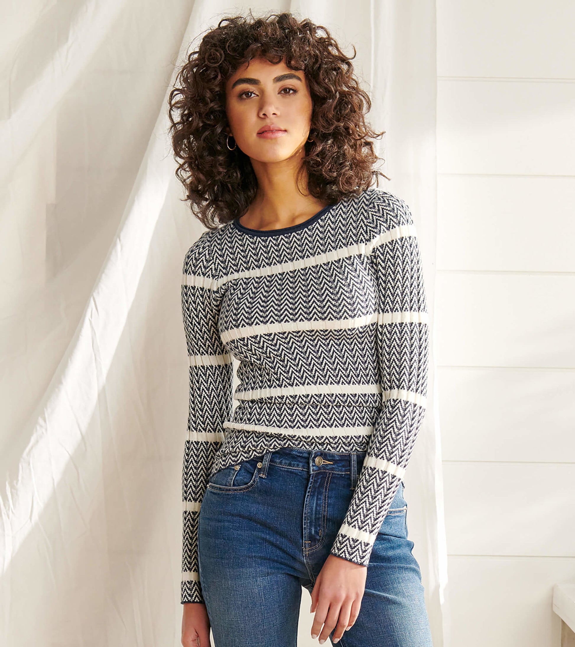 Navy and white zigzag patterned sweater with long sleeves, paired with blue jeans.
